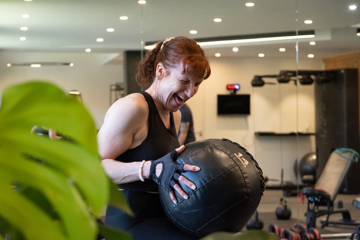 Une adhérente rit en plein effort avec un medecine-ball, dans un studio My Coach.