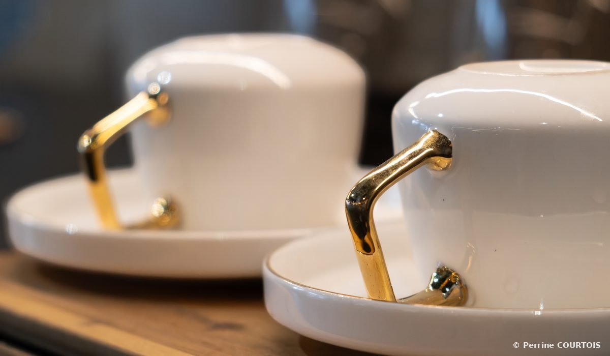 Deux tasses blanches à anses dorées posées sur leurs soucoupes.