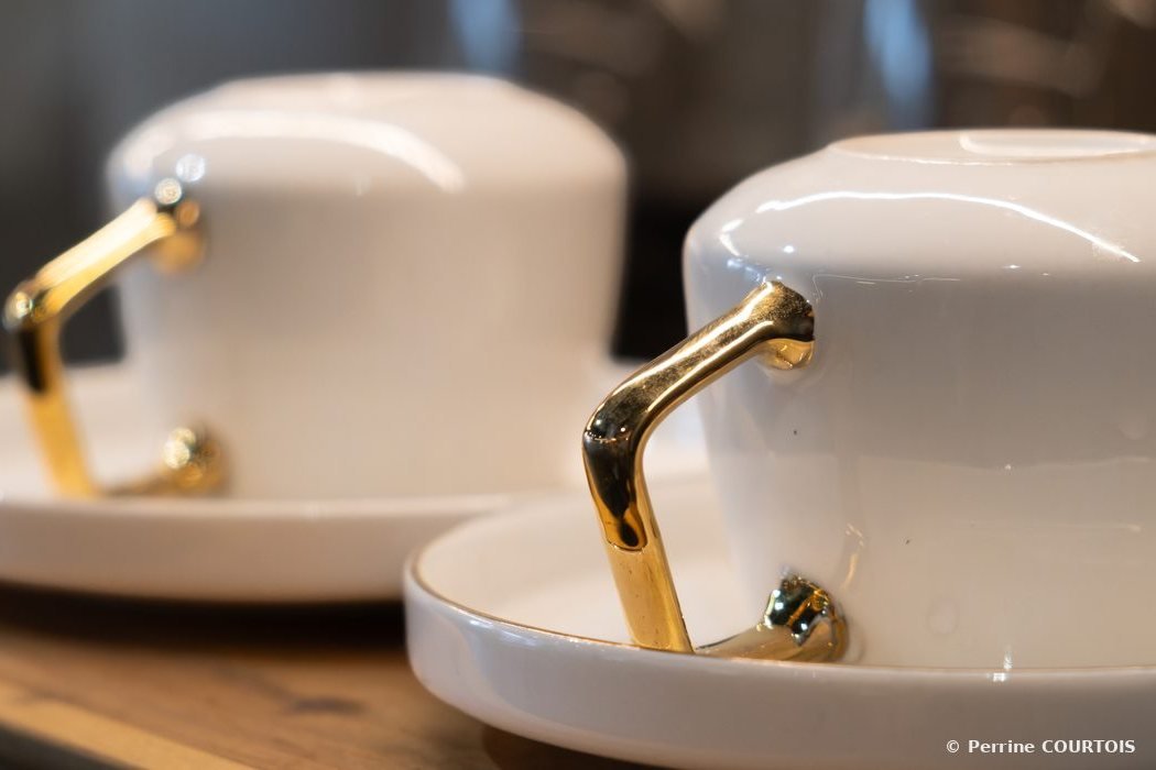 Deux tasses blanches à anses dorées posées sur leurs soucoupes.