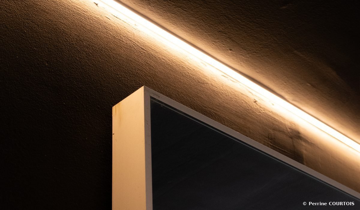 Angle d'un miroir à cadre blanc sous un ruban lumineux, sur un mur sombre.