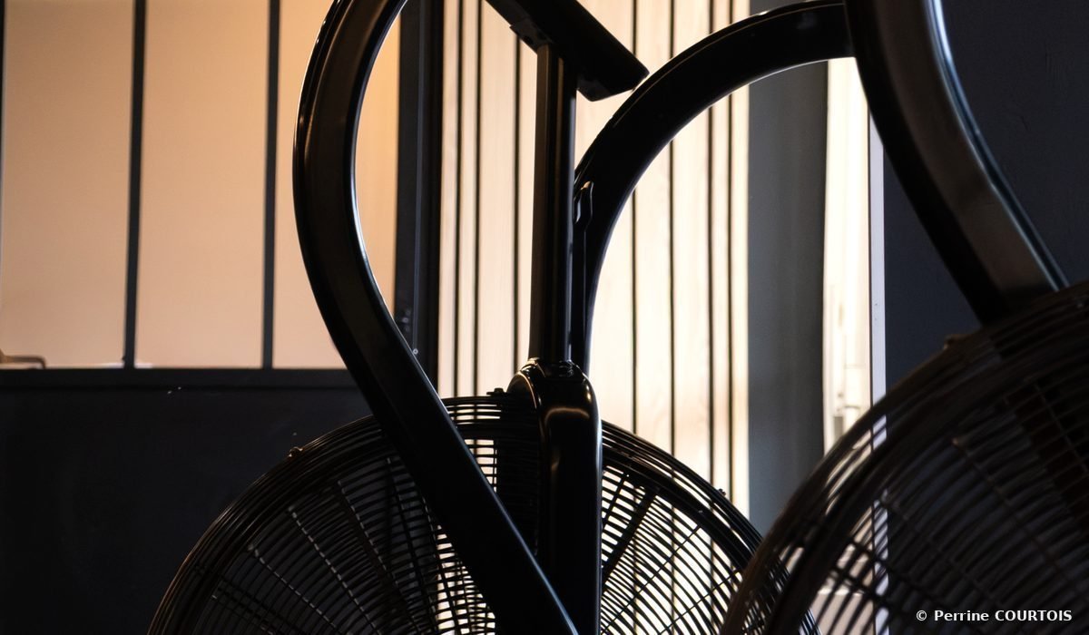 Deux vélos à air noirs devant une verrière et des tasseaux de bois.