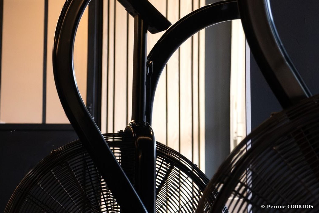 Deux vélos à air noirs devant une verrière et des tasseaux de bois.