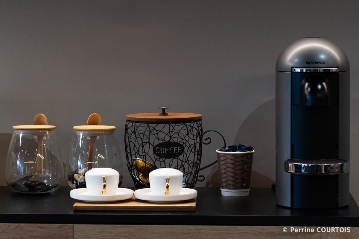 Coin café : machine à café, tasses blanches, bocaux en verre et pot à café sur un meuble sombre.