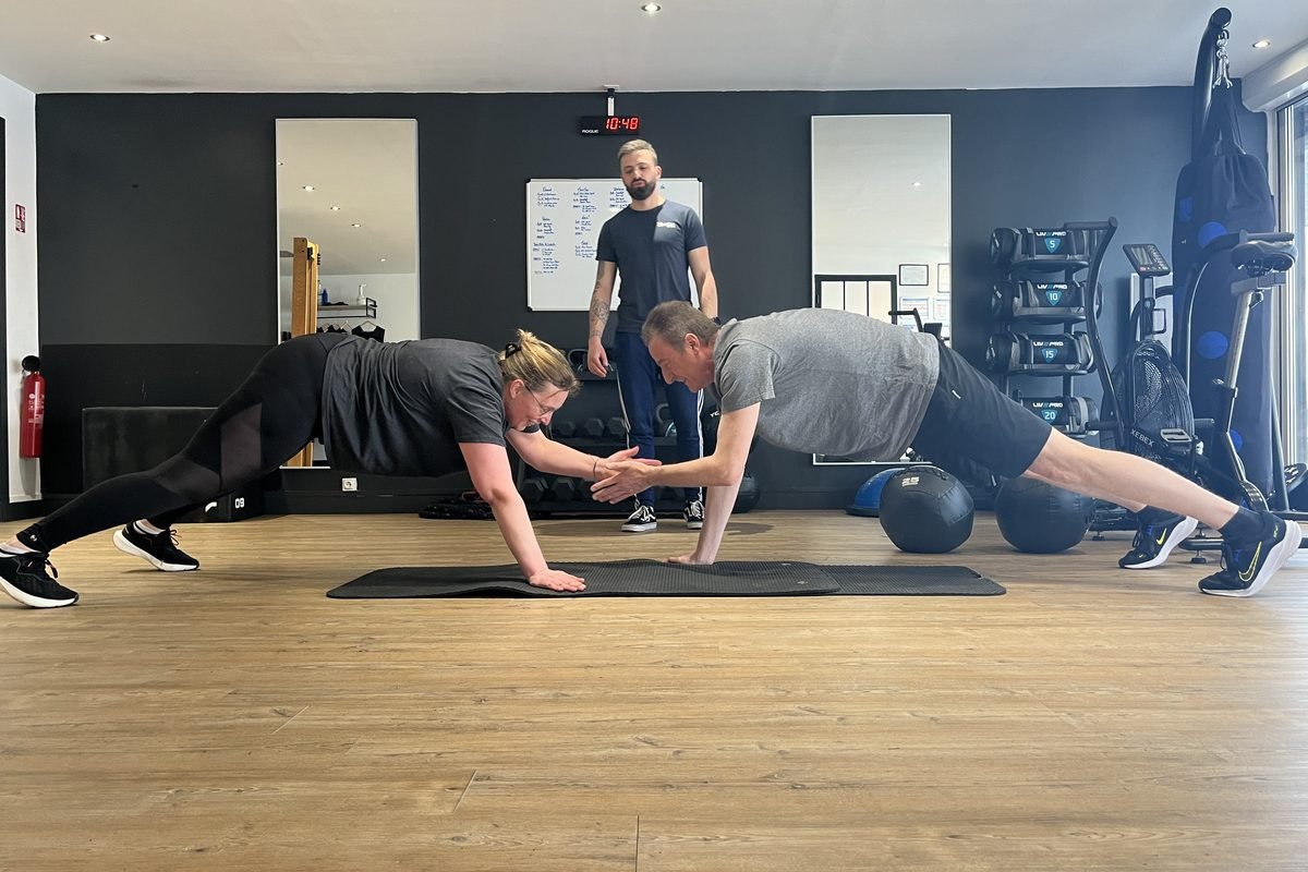 Deux adhérents en planche se tapent dans la main sous le regard de leur coach, au studio de Marcq-en-Barœul.