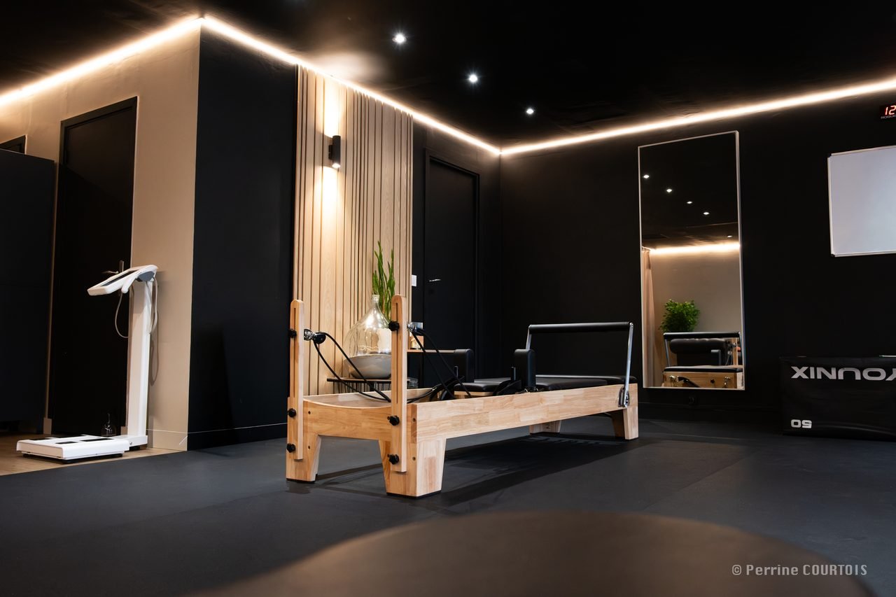 Un studio My Coach prêt à accueillir ses premiers clients : reformer de Pilates au centre, éclairage indirect, murs sombres et bois clair.