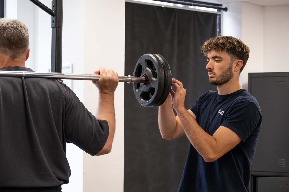Un coach accompagne un adhérent pendant un exercice avec barre, au studio de Levallois-Perret.