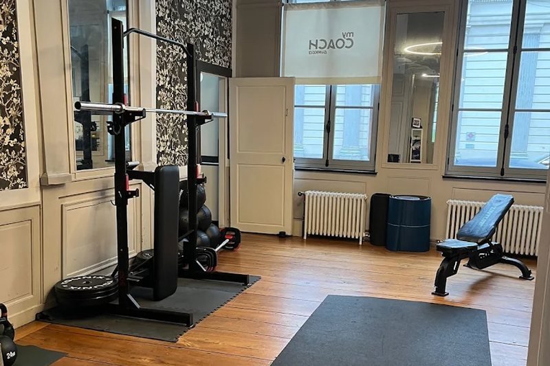 La salle d'entraînement du studio de Lille, avec rack, banc, tapis et vitrage aux couleurs My Coach.