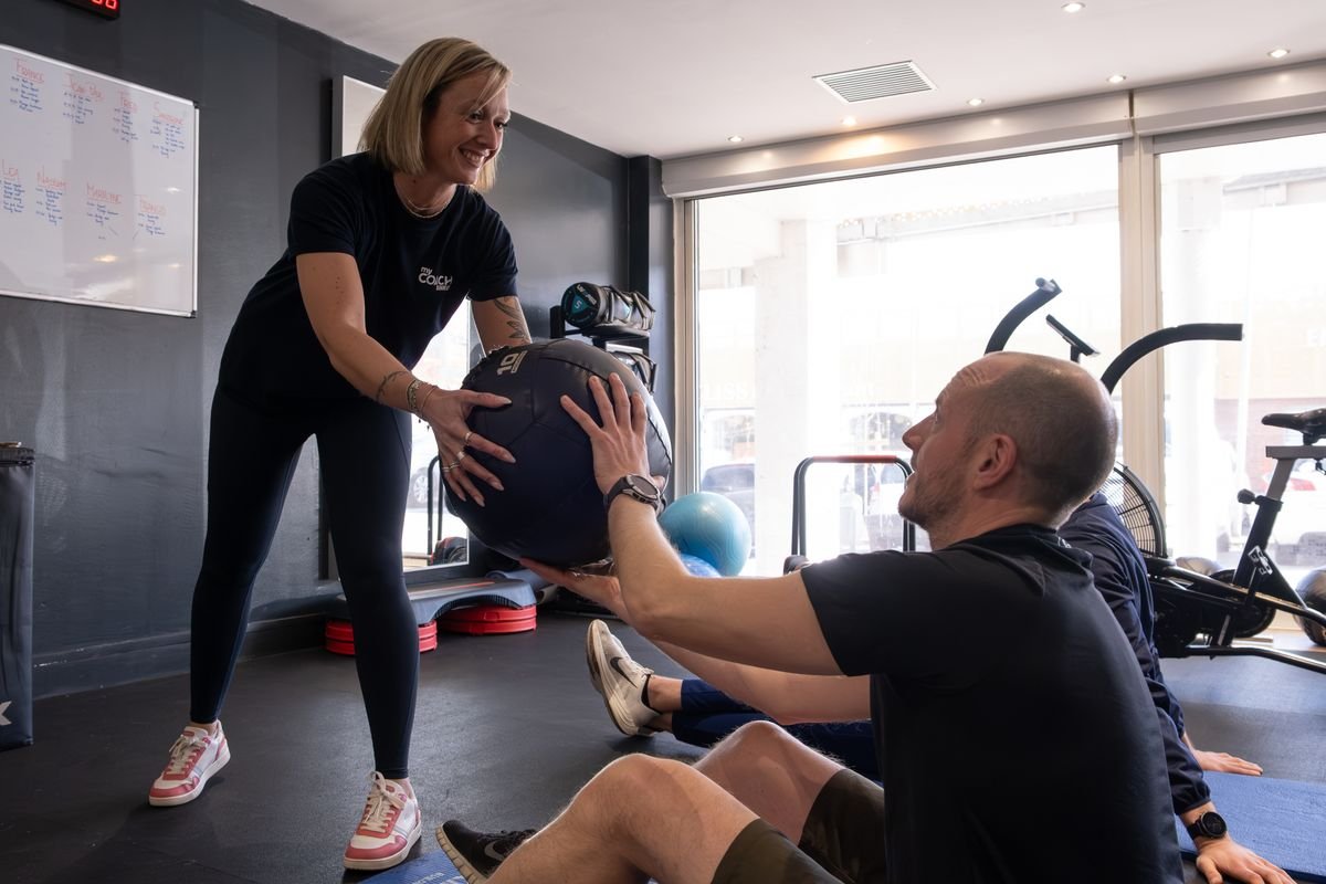 Une coach accompagne un adhérent pendant un exercice au medecine-ball, au studio de Marcq-en-Barœul.