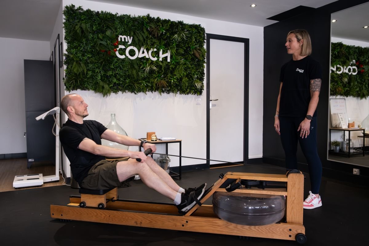 Un adhérent sur le rameur, suivi par sa coach, au studio de Marcq-en-Barœul.